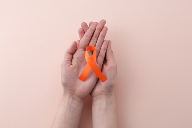 Woman with orange awareness ribbon on beige background, top view