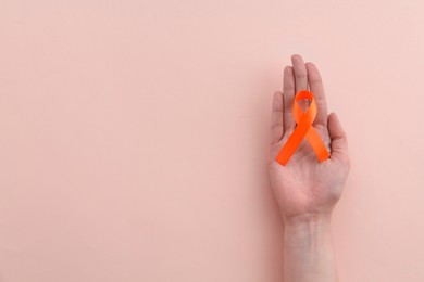 Photo of Woman with orange awareness ribbon on beige background, top view. Space for text