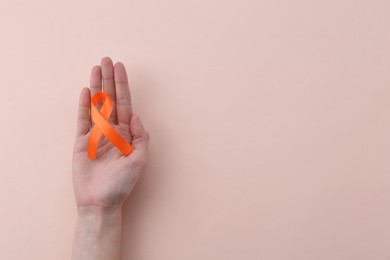 Woman with orange awareness ribbon on beige background, top view. Space for text