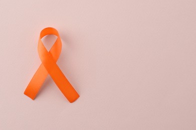 Photo of Orange awareness ribbon on beige background, top view. Space for text