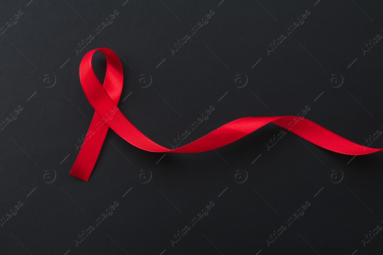 Photo of Red awareness ribbon on black background, top view