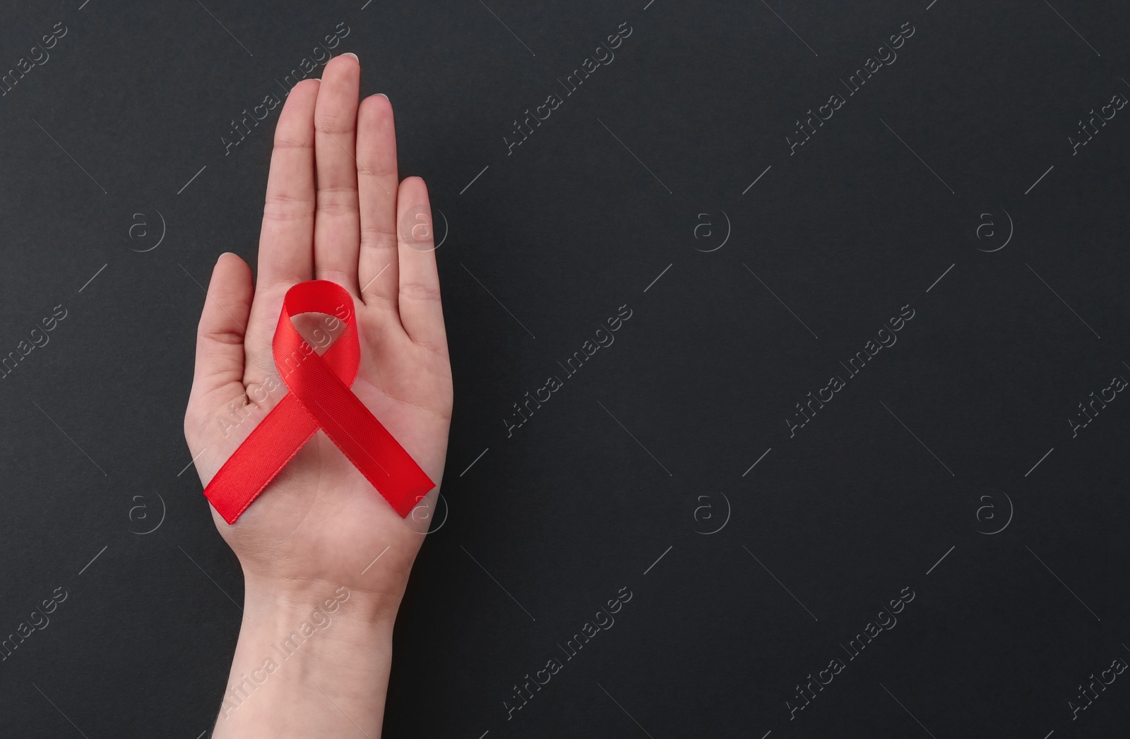 Photo of Woman with red awareness ribbon on black background, top view. Space for text