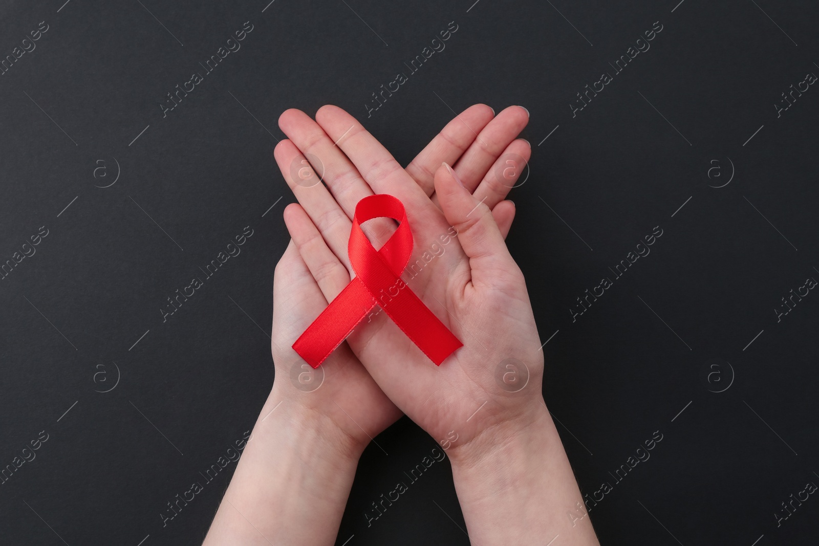 Photo of Woman with red awareness ribbon on black background, top view