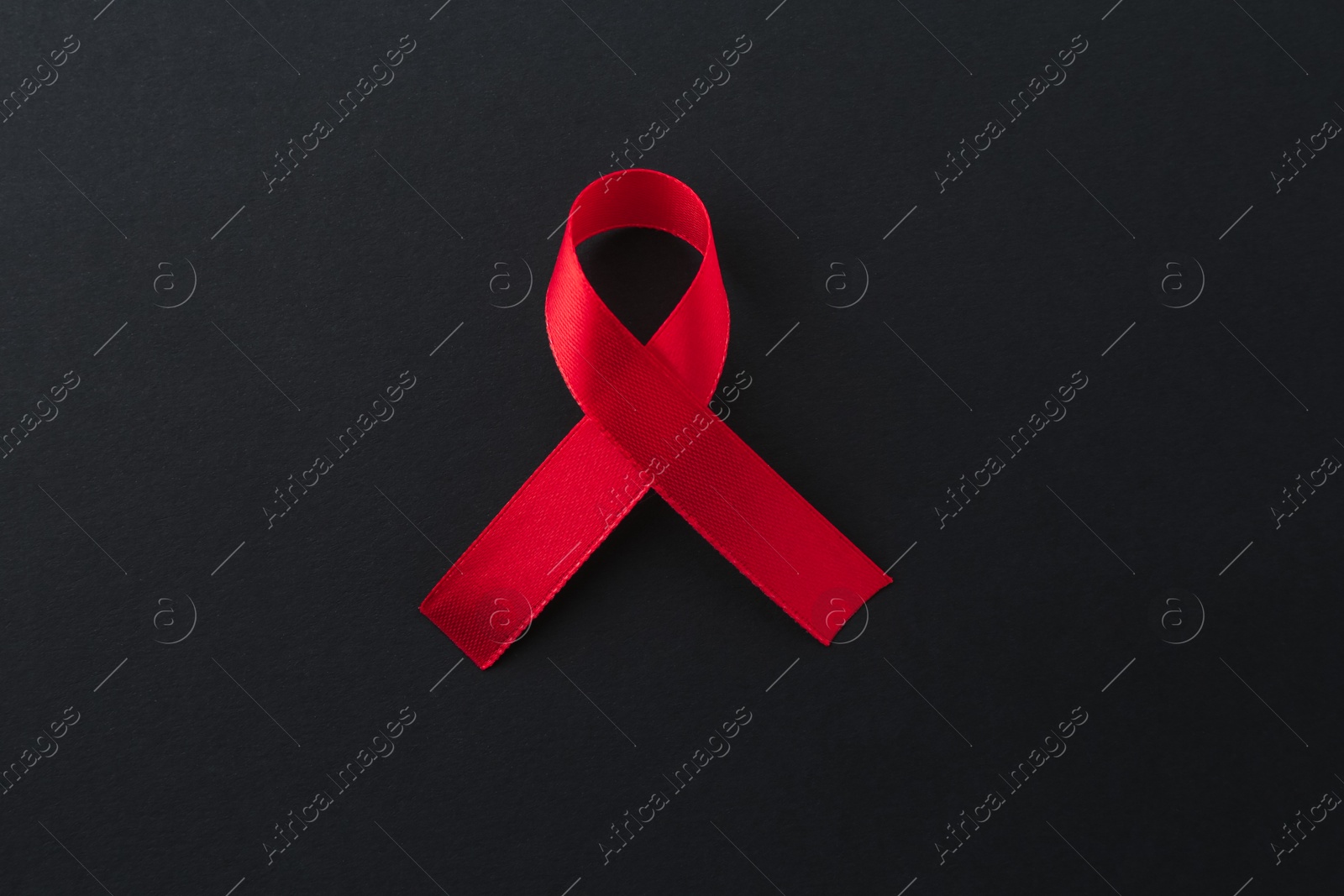 Photo of Red awareness ribbon on black background, top view