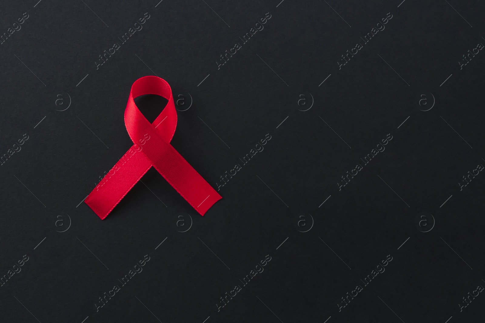 Photo of Red awareness ribbon on black background, top view. Space for text