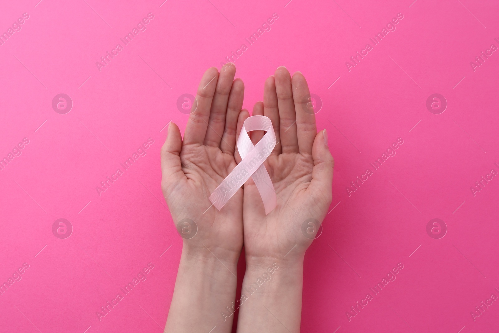 Photo of Woman with awareness ribbon on pink background, top view