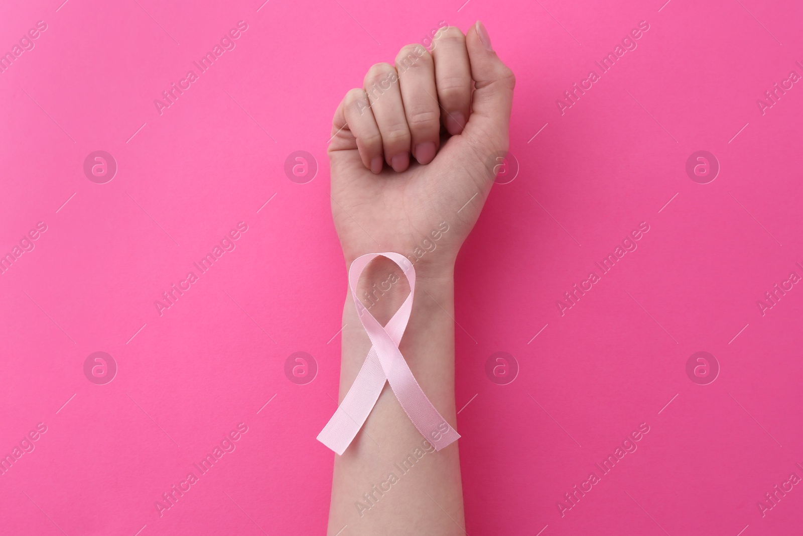 Photo of Woman with awareness ribbon on pink background, top view