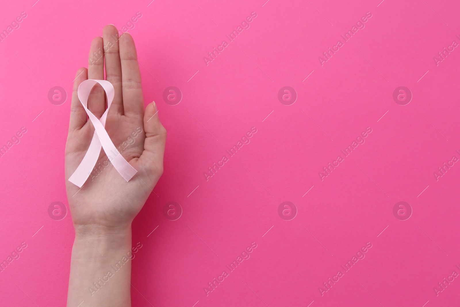 Photo of Woman with awareness ribbon on pink background, top view. Space for text