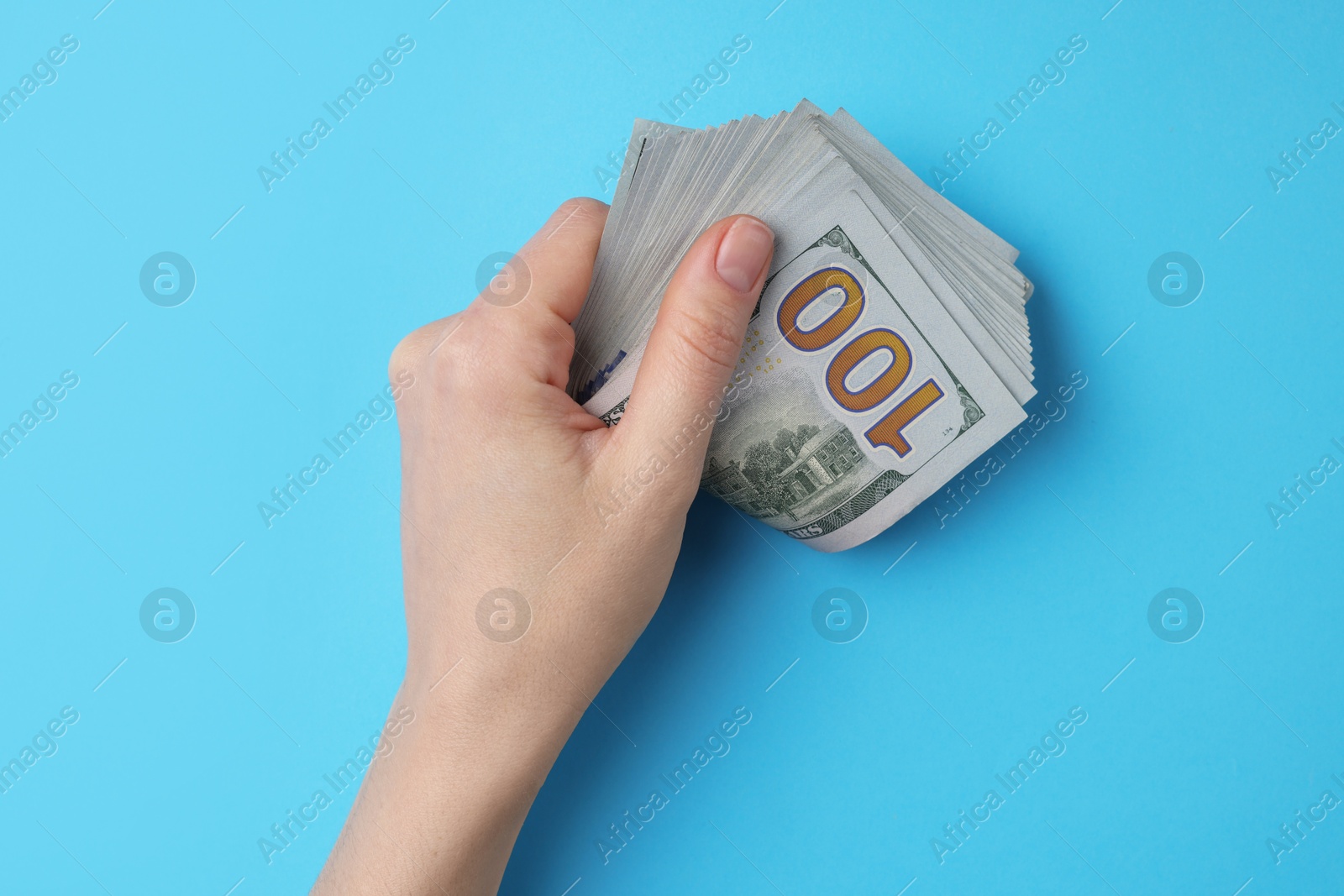 Photo of Money exchange. Woman holding dollar banknotes on light blue background, top view