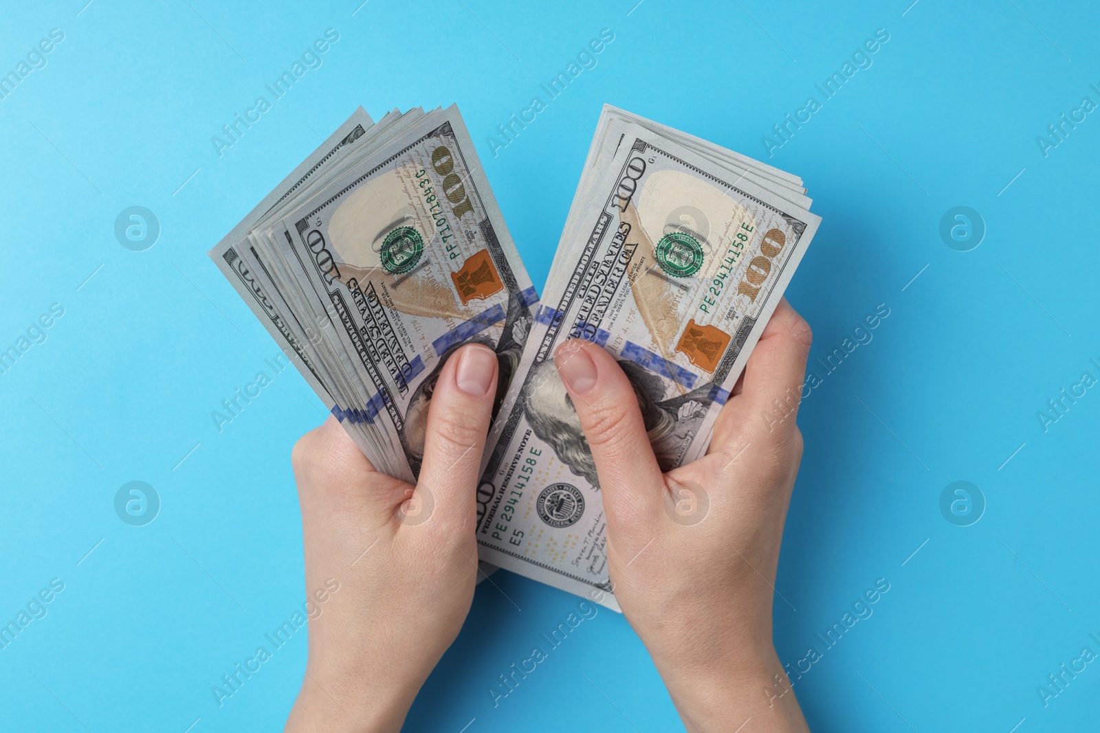 Photo of Money exchange. Woman holding dollar banknotes on light blue background, top view