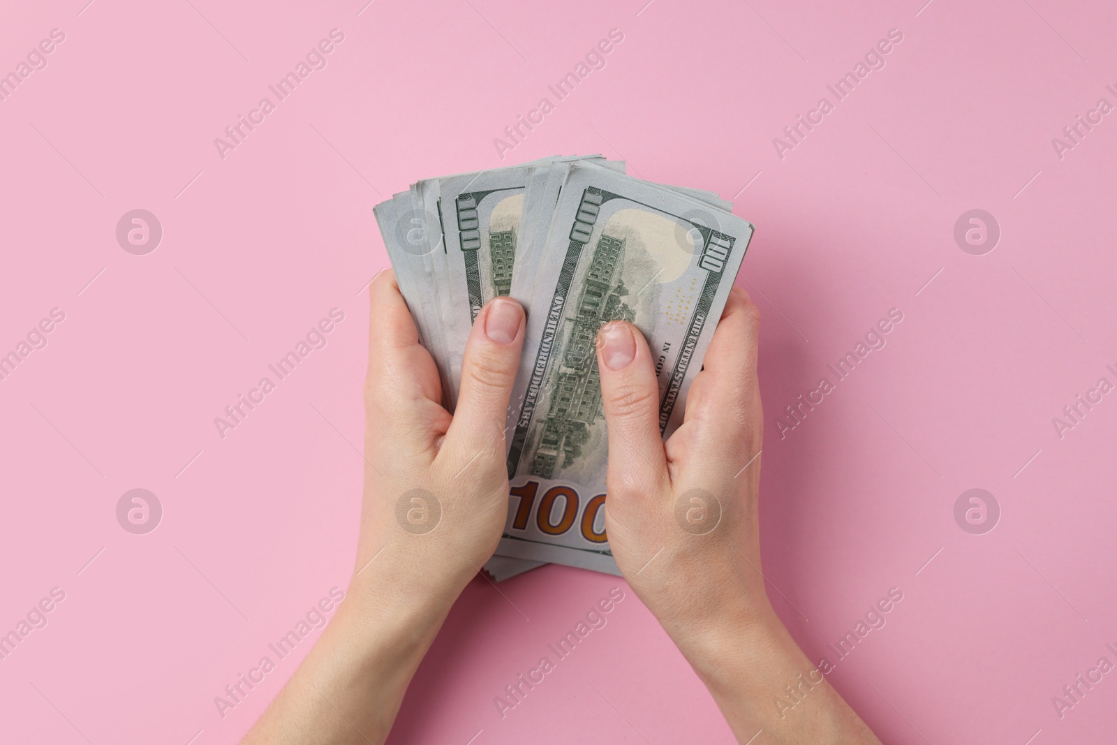 Photo of Money exchange. Woman holding dollar banknotes on pink background, top view