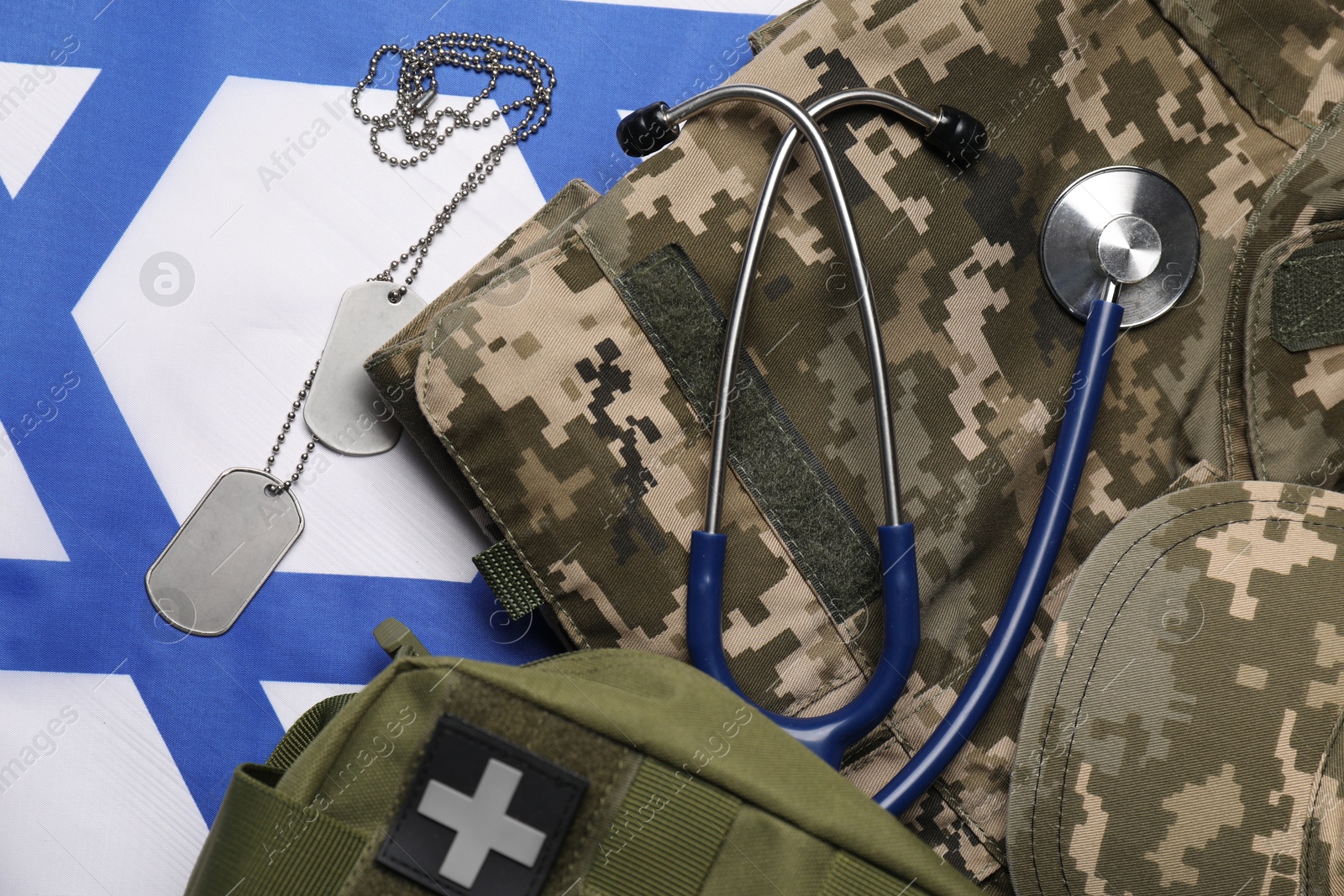 Photo of Stethoscope, first aid kit, tags and military uniform on flag of Israel, flat lay