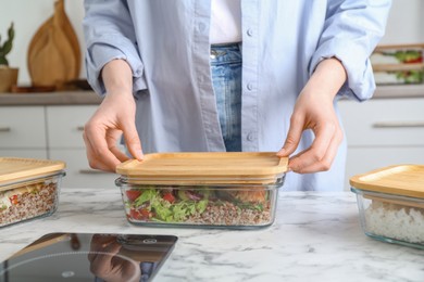 Healthy food. Woman closing glass container with meal at white marble table, closeup