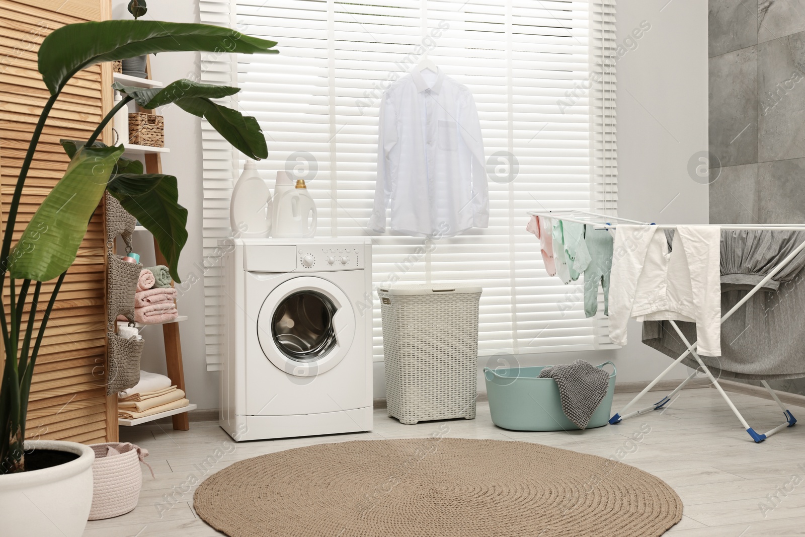 Photo of Washing machine, detergents, towels, baskets and drying rack in laundry room