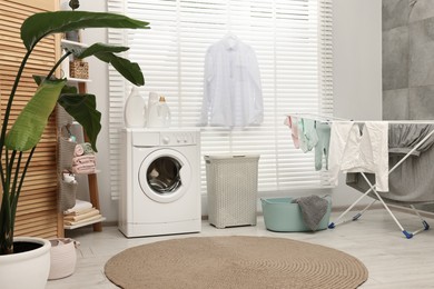 Photo of Washing machine, detergents, towels, baskets and drying rack in laundry room