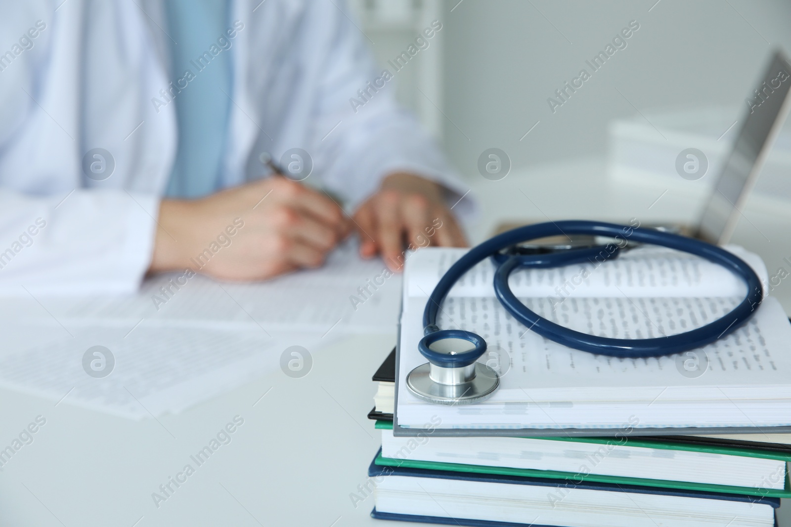 Photo of Doctor at white table in hospital, focus on medical stethoscope and books