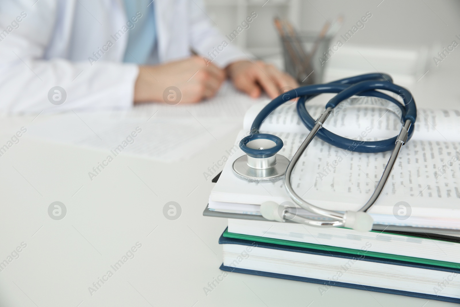 Photo of Doctor at white table in hospital, focus on medical stethoscope and books