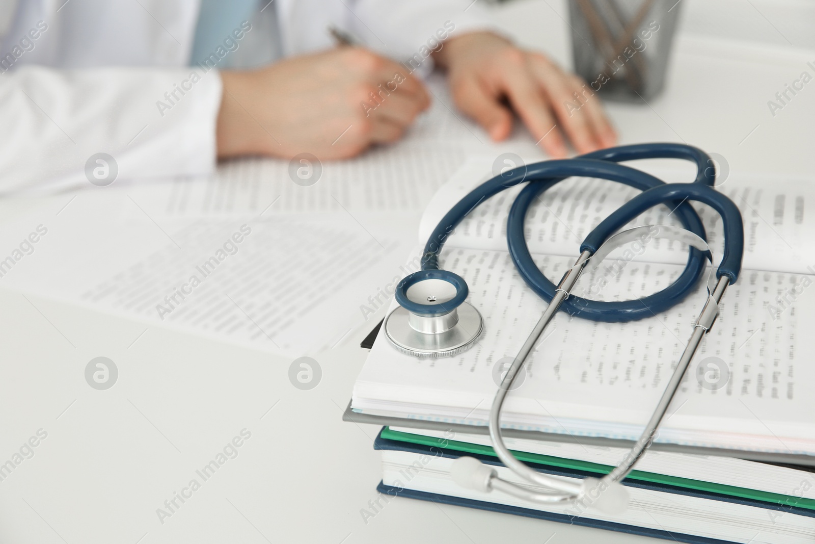 Photo of Doctor at white table in hospital, focus on medical stethoscope and books