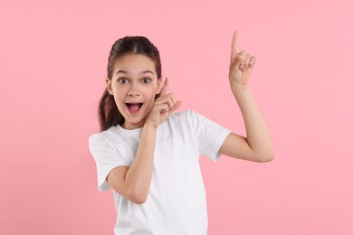 Photo of Portrait of emotional girl pointing at something on pink background