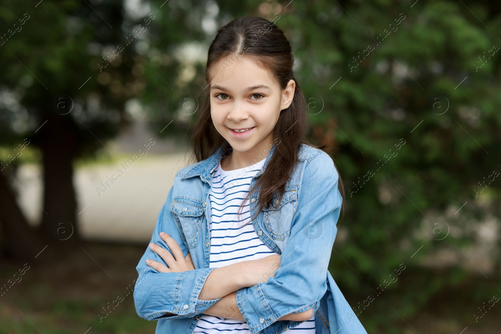 Photo of Portrait of happy little girl with crossed arms outdoors