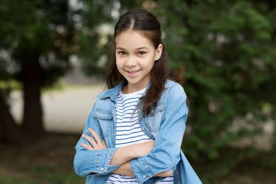 Portrait of happy little girl with crossed arms outdoors