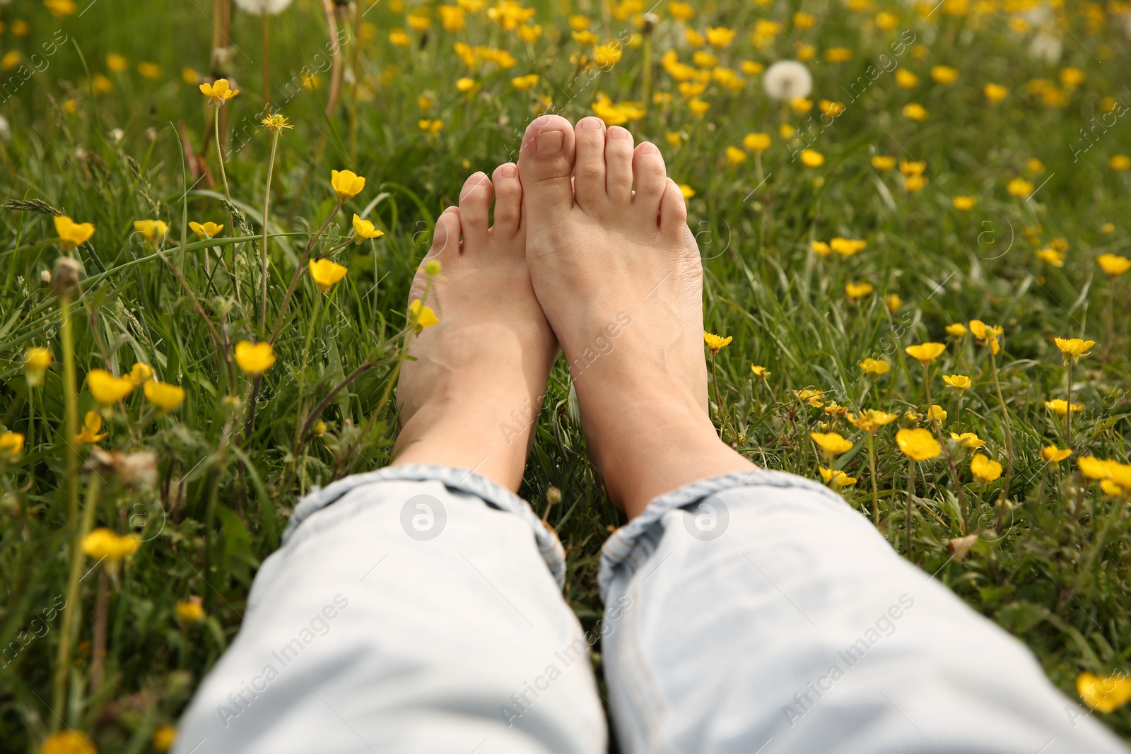 Photo of Woman sitting barefoot on green grass outdoors, closeup