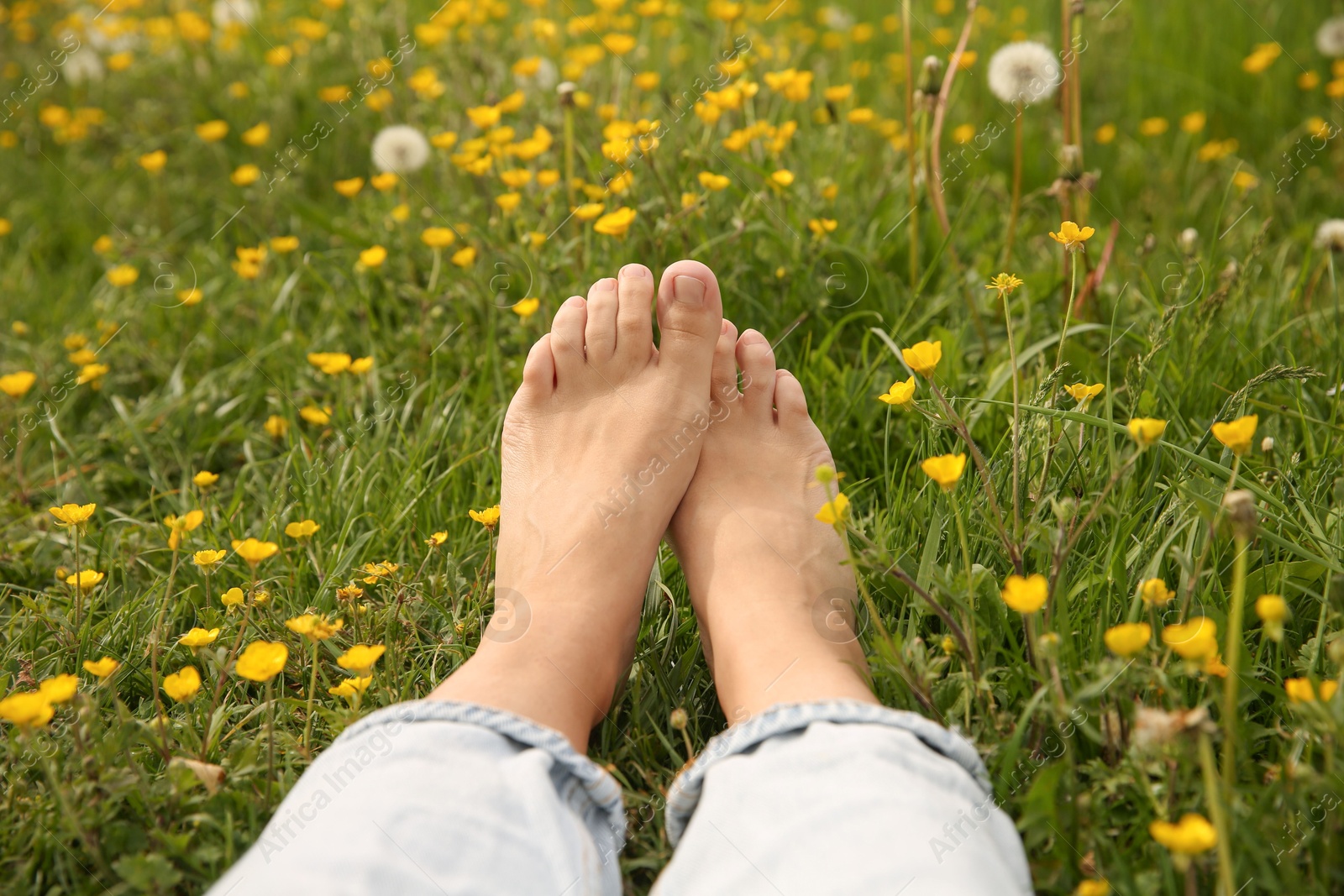 Photo of Woman sitting barefoot on green grass outdoors, closeup