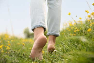 Photo of Woman walking barefoot on green grass outdoors, closeup