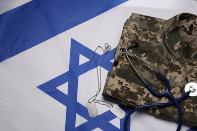 Stethoscope, tags and military uniform on flag of Israel, flat lay