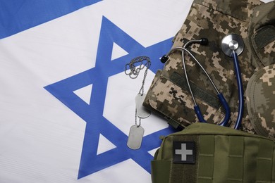 Stethoscope, first aid kit, tags and military uniform on flag of Israel, flat lay