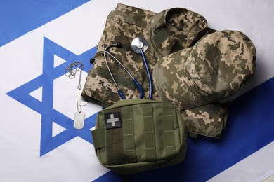 Photo of Stethoscope, first aid kit, tags and military uniform on flag of Israel, flat lay