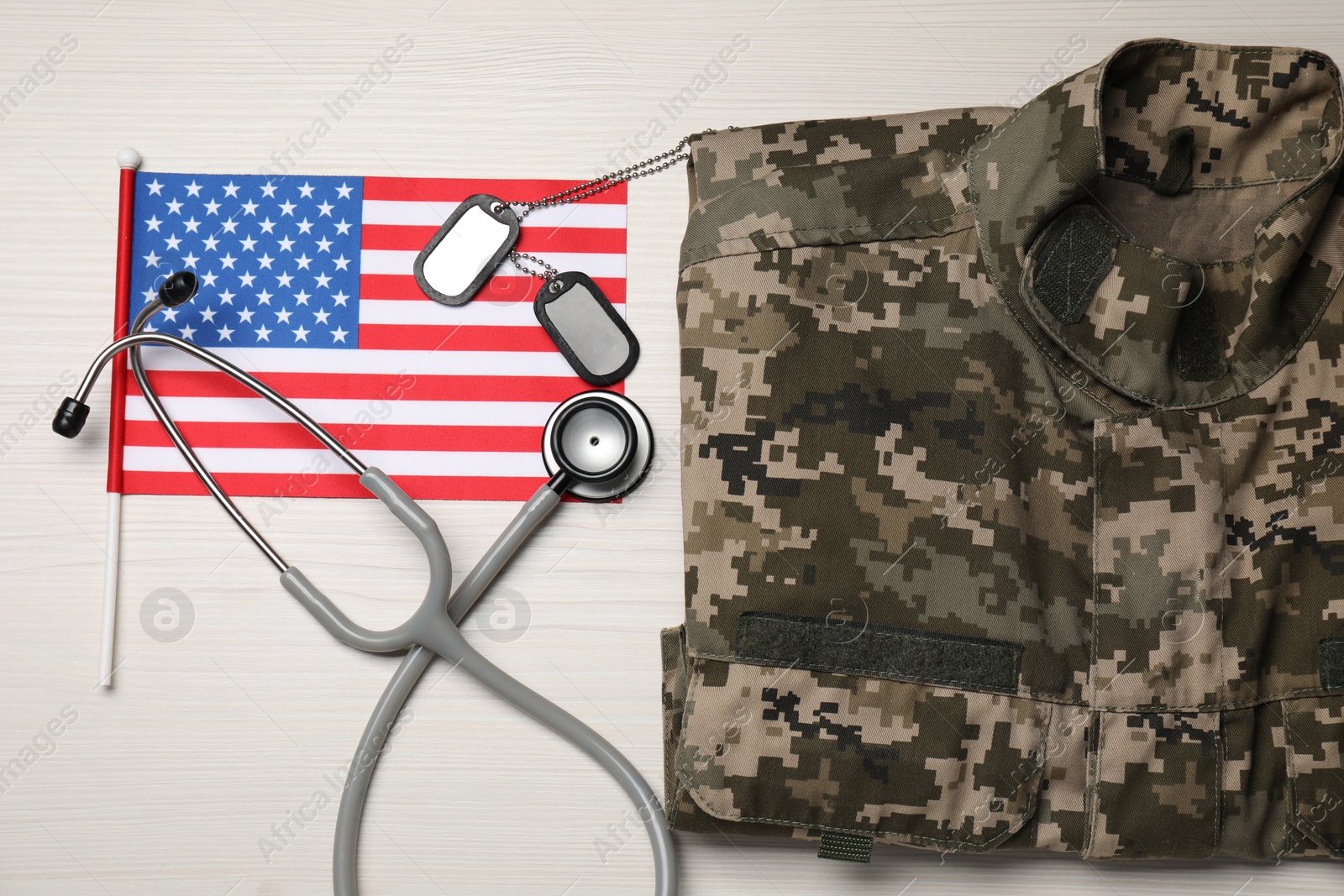 Photo of Stethoscope, USA flag, tags and military uniform on white wooden table, flat lay