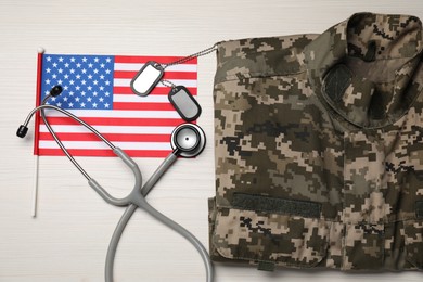 Stethoscope, USA flag, tags and military uniform on white wooden table, flat lay