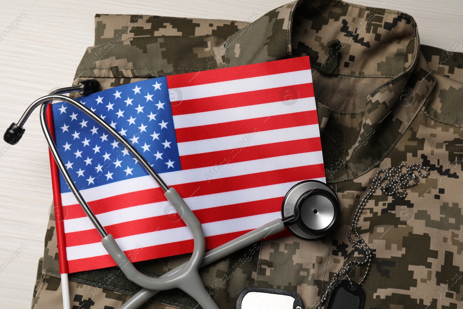 Photo of Stethoscope, USA flag, tags and military uniform on white wooden table, top view