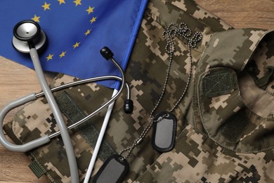 Stethoscope, flag of European Union, tags and military uniform on wooden table, flat lay