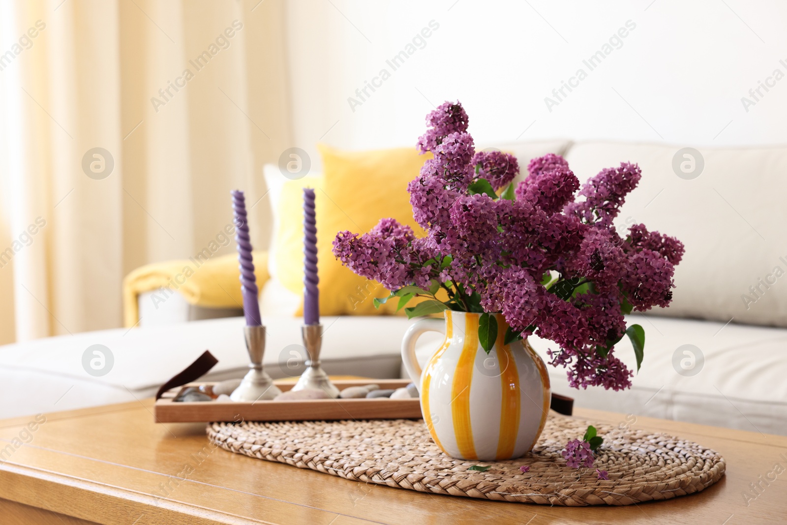 Photo of Beautiful fragrant lilac flowers in vase and candles on table at home