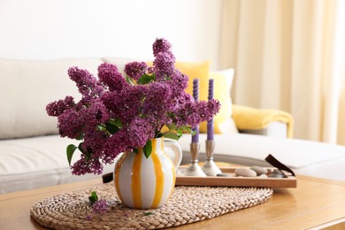 Beautiful fragrant lilac flowers in vase and candles on table at home. Space for text