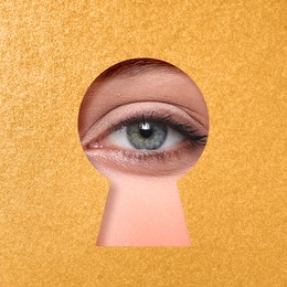 Woman looking through keyhole in golden surface