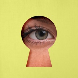 Woman looking through keyhole in color surface