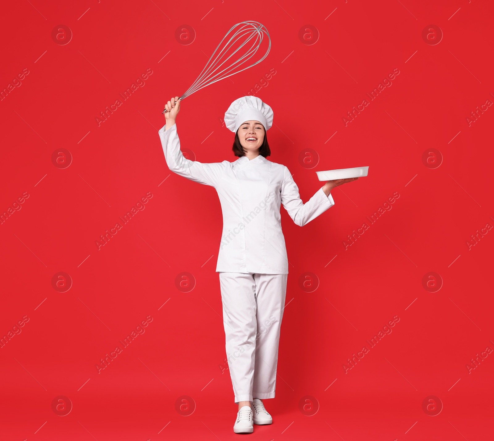 Image of Happy pastry chef with big whisk and dishware on red background