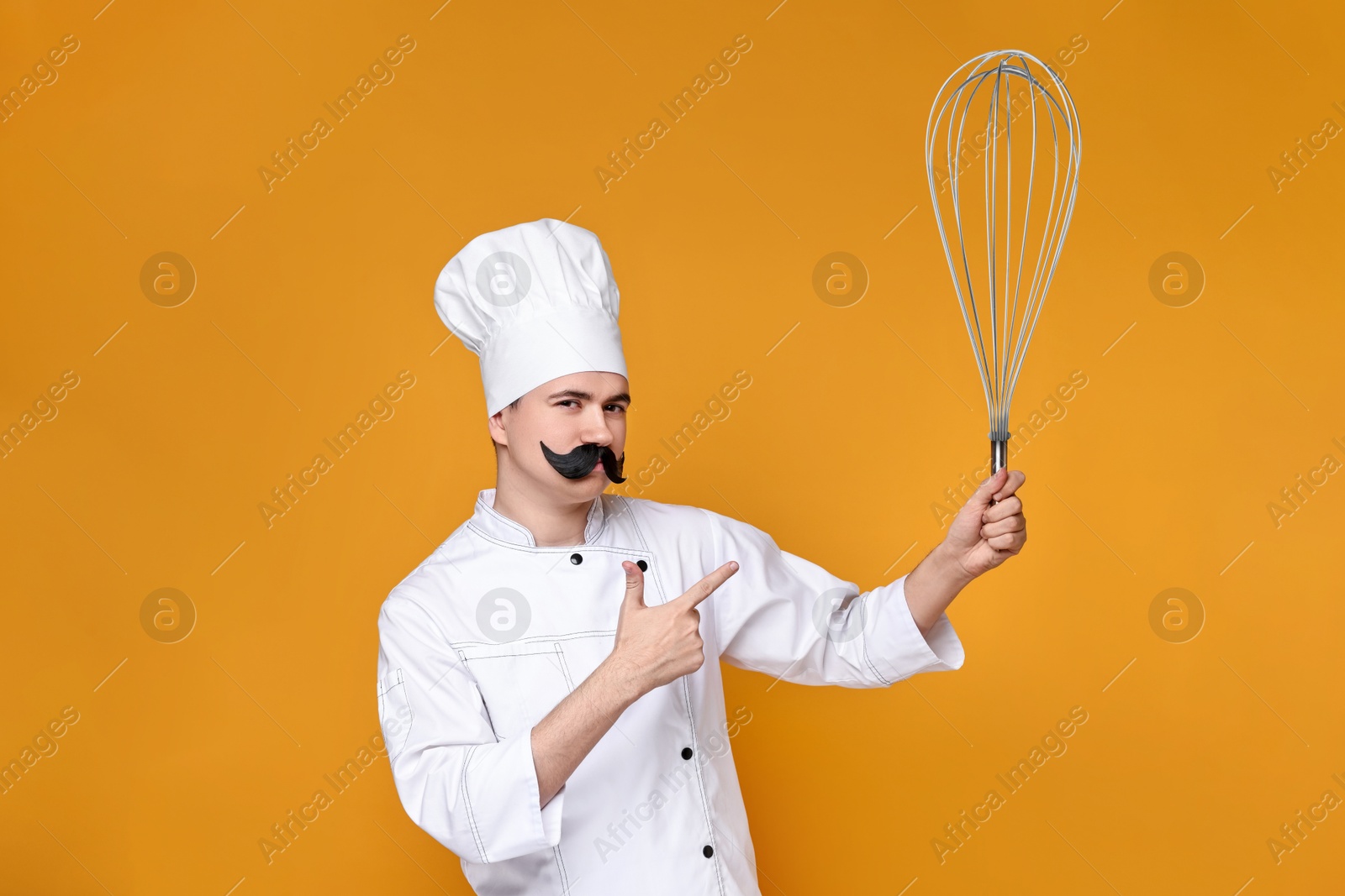 Image of Pastry chef with fake mustache pointing at big whisk on orange background
