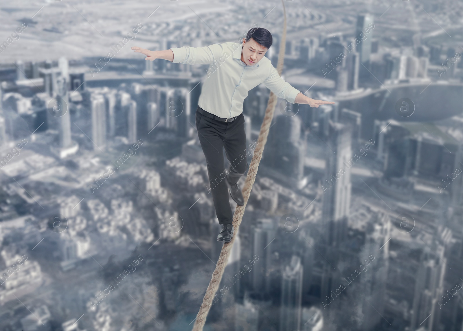 Image of Concentrated businessman walking rope over city. Concept of risk and balance