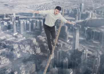 Concentrated businessman walking rope over city. Concept of risk and balance