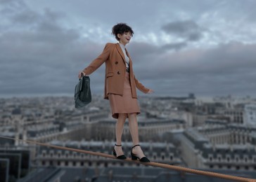 Businesswoman walking rope over city. Concept of risk and balance