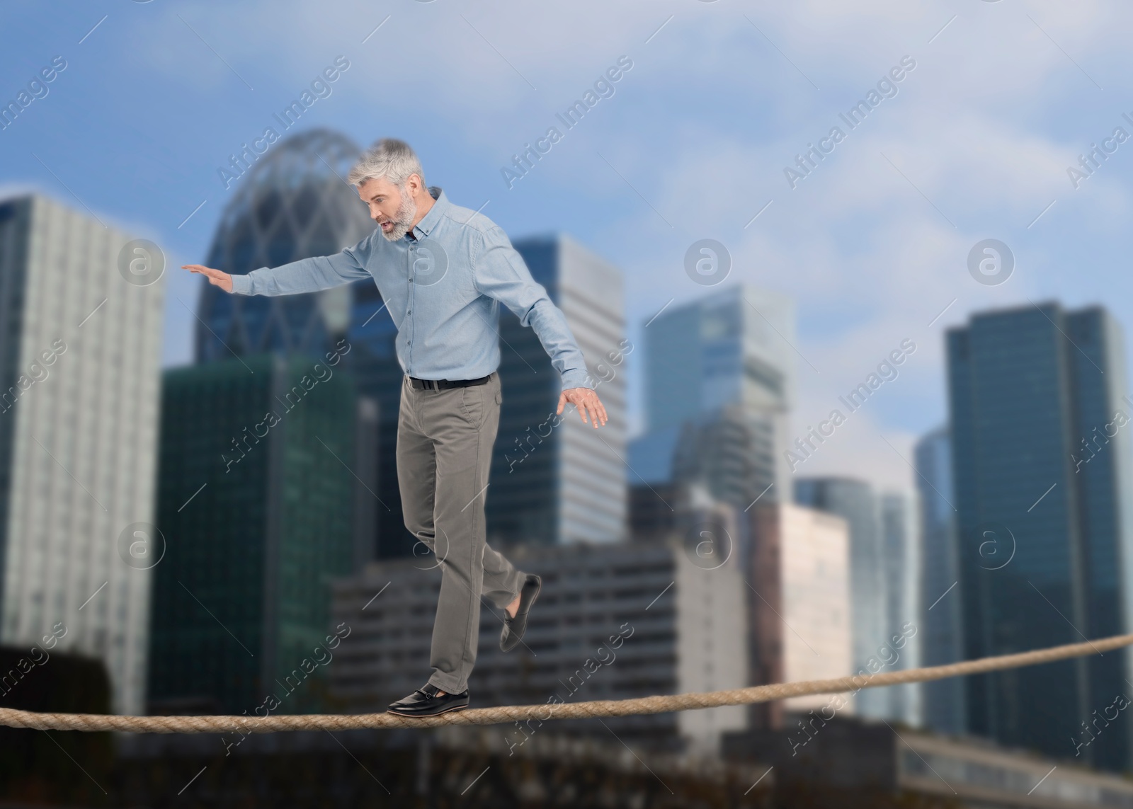 Image of Concentrated businessman walking rope over city. Concept of risk and balance