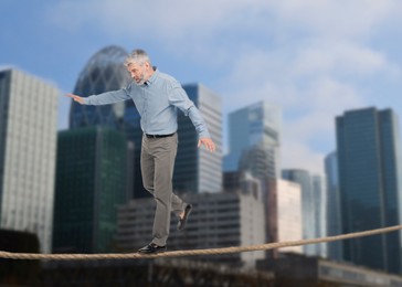 Concentrated businessman walking rope over city. Concept of risk and balance