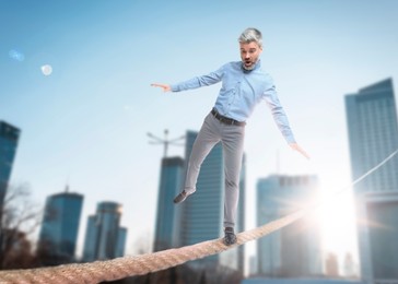 Image of Concentrated businessman balancing on rope over city. Concept of risk