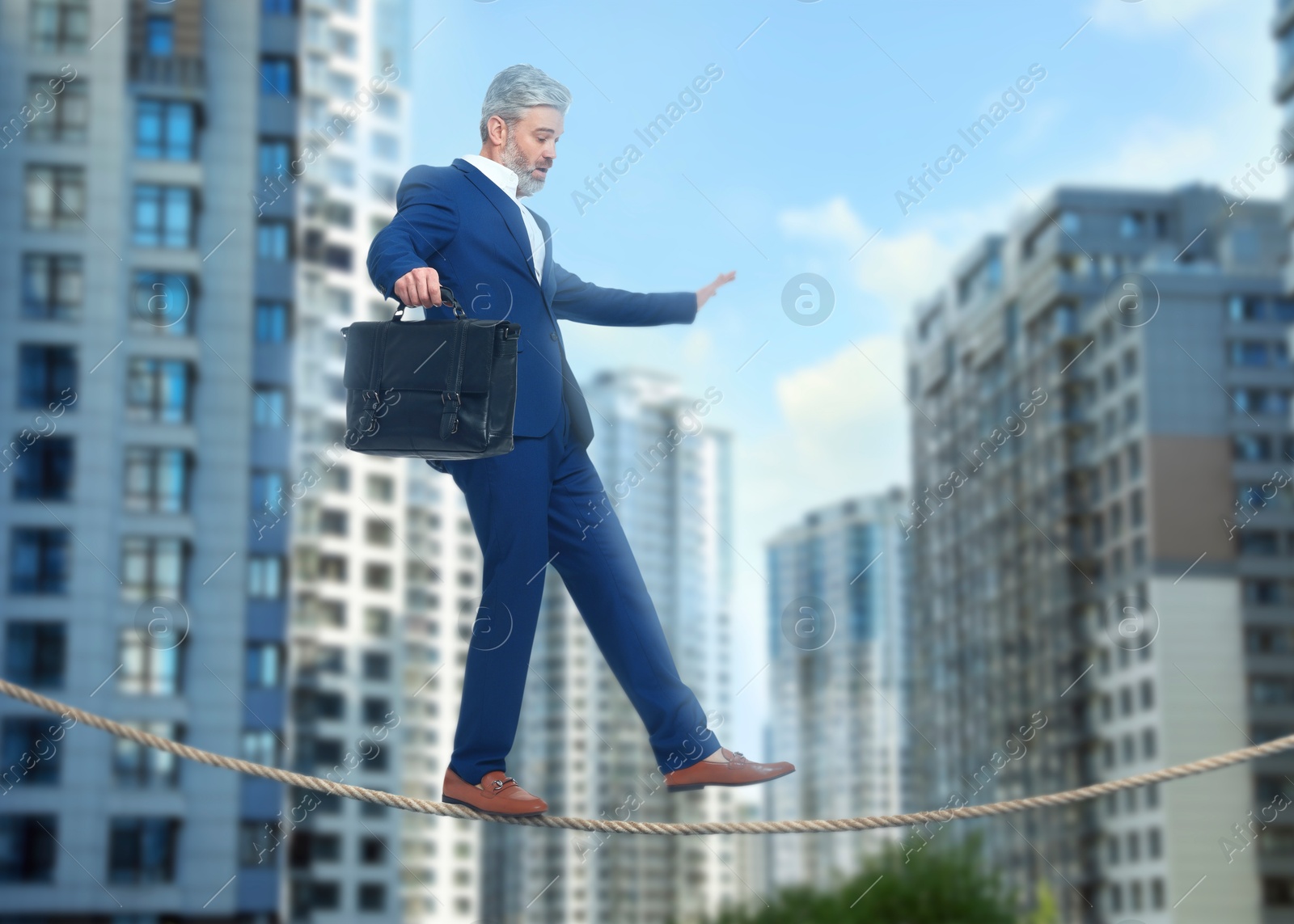 Image of Concentrated businessman walking rope over city. Concept of risk and balance