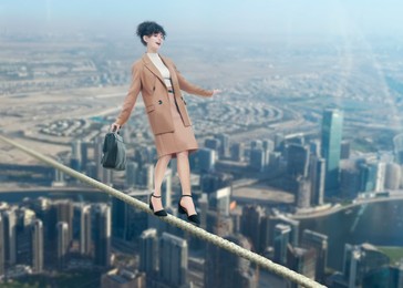 Image of Businesswoman walking rope over city. Concept of risk and balance
