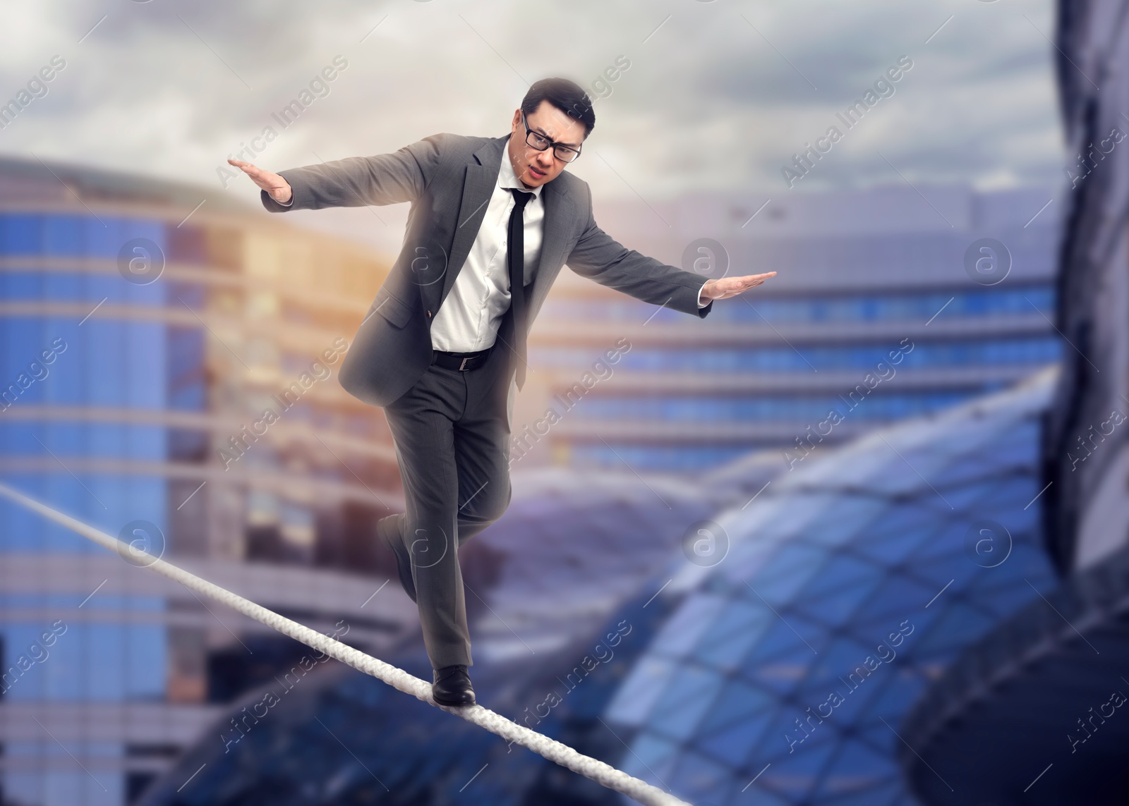 Image of Concentrated businessman walking rope over city. Concept of risk and balance